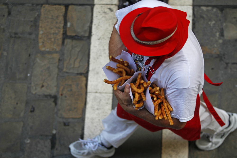 Un mozo sanferminero lleva 3 cucuruchos de churros recién hechos