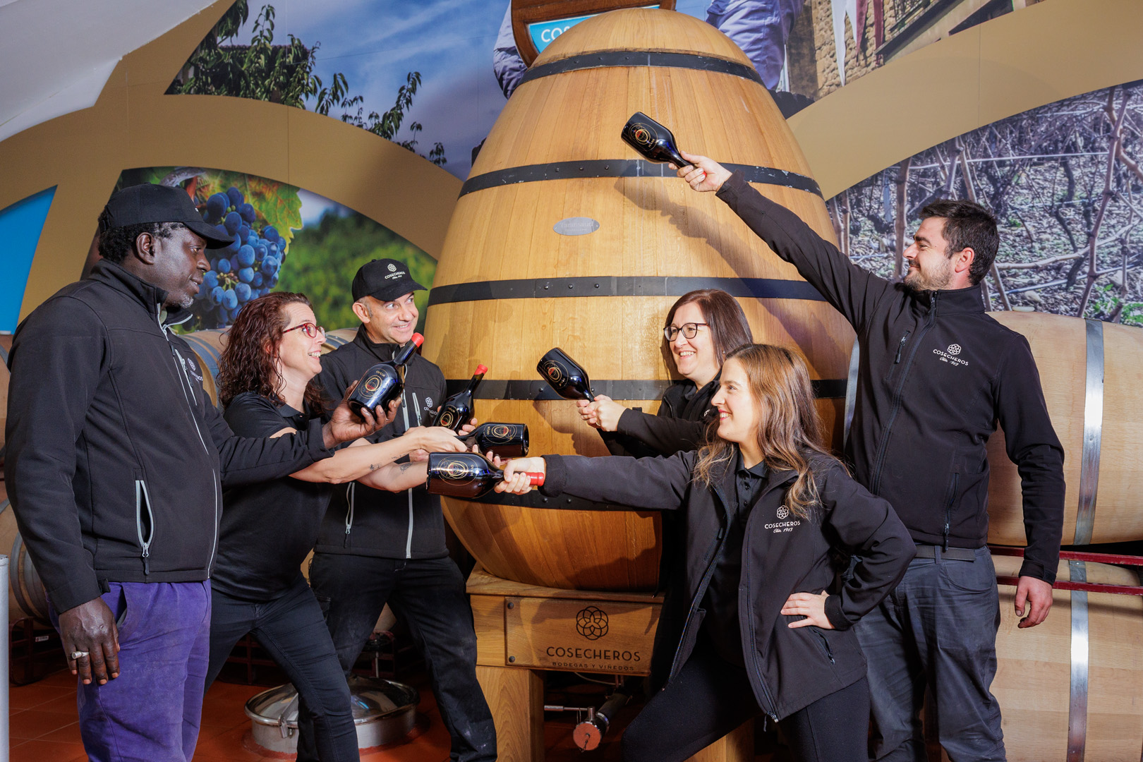 Grupo de personas con una botella de vino delante de una barrica
