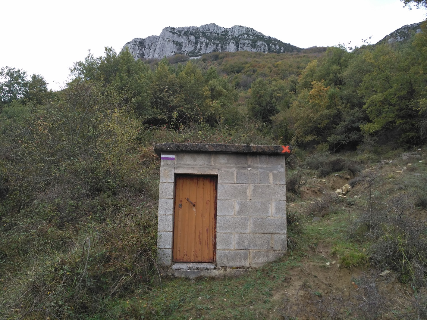 caseta de bloques al lado del camino y al fondo la peña