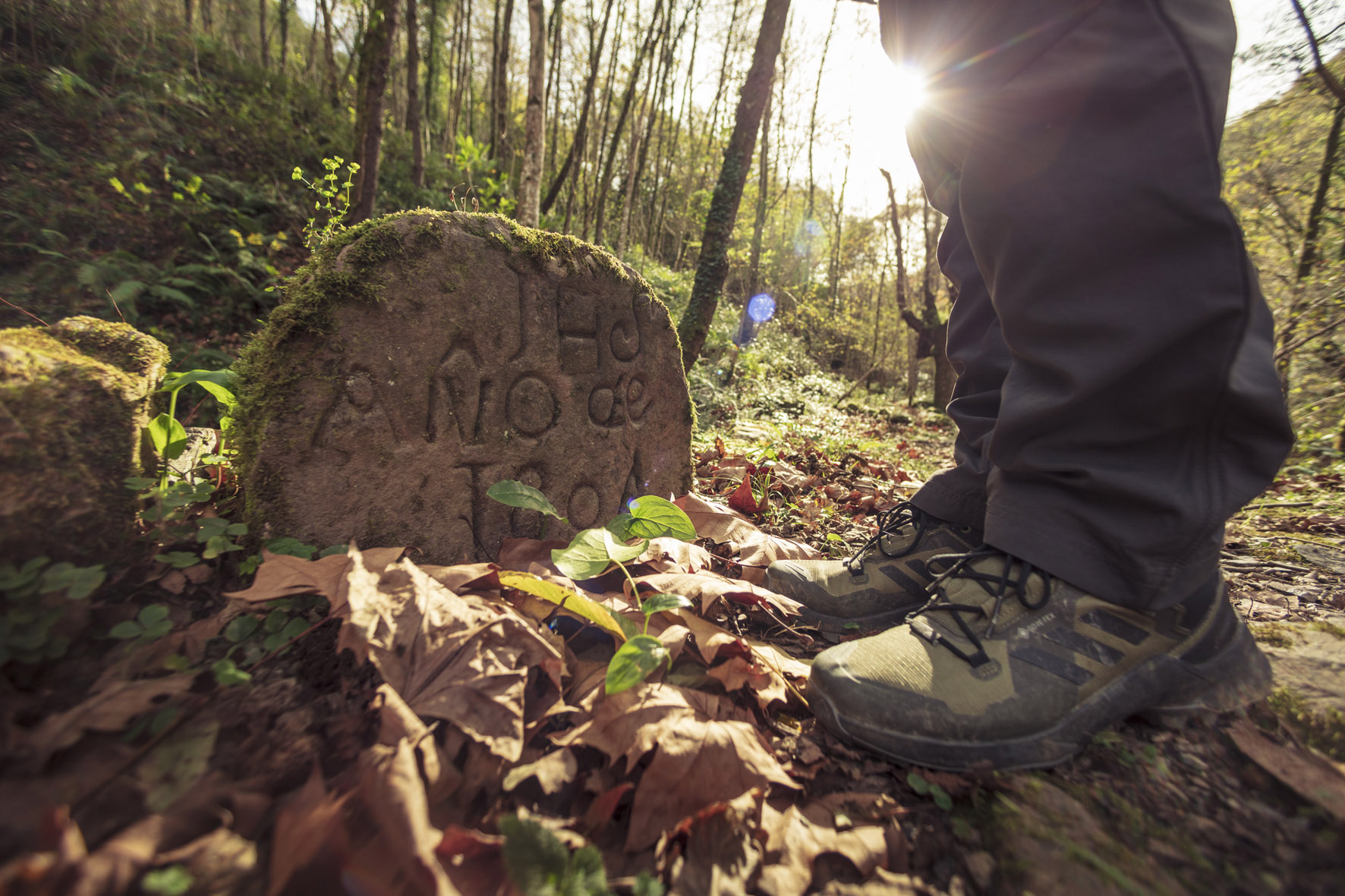 piedra con letras en el suelo y botas de monte y piernas de un hombre