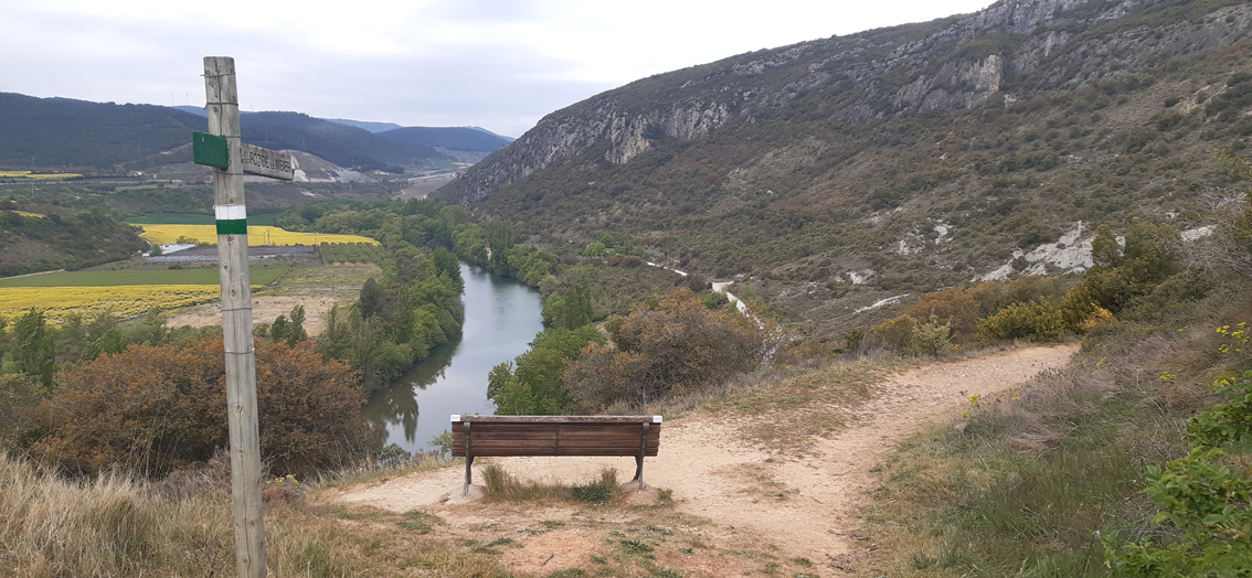vista del río con poste del sendero y banco de madera