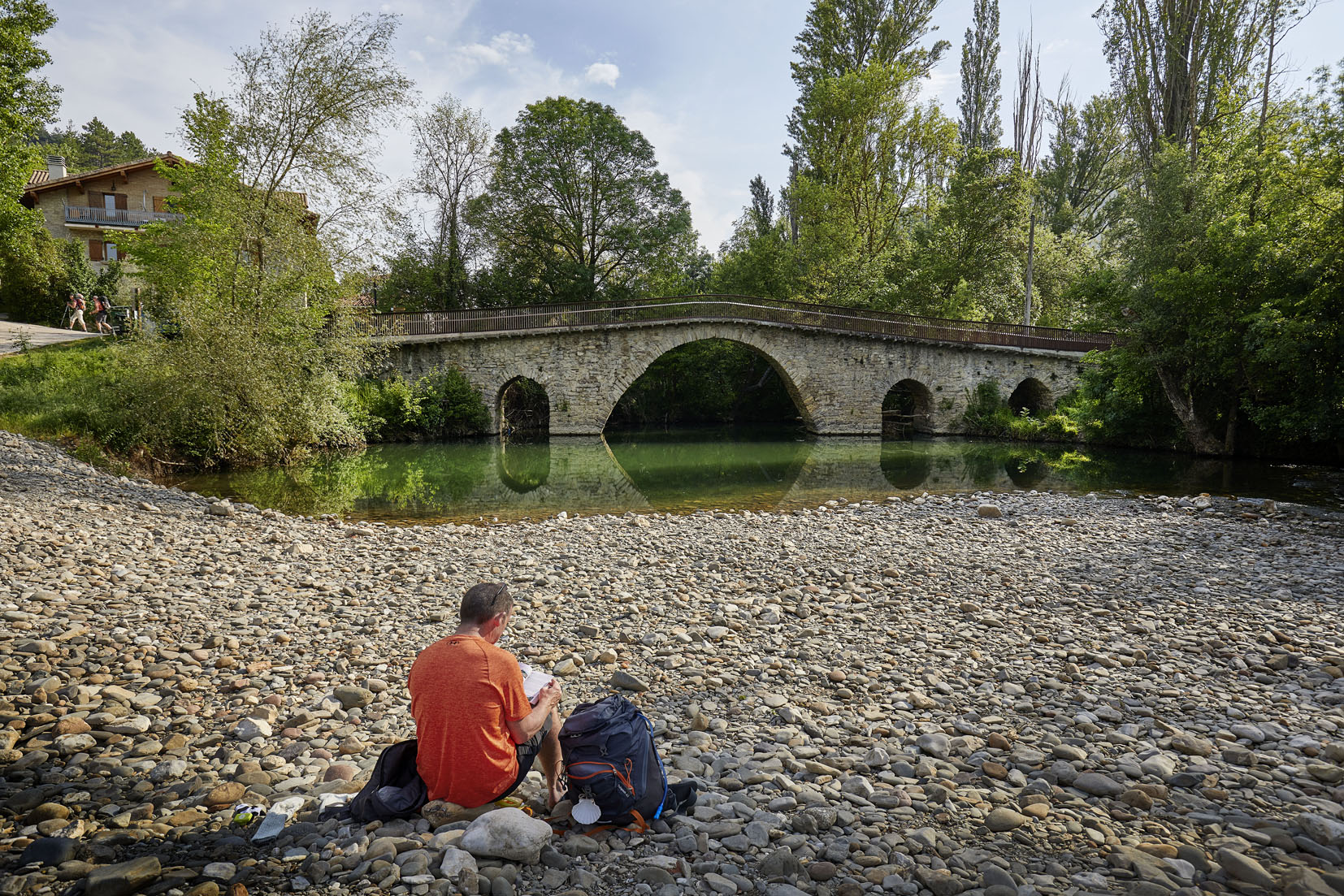 peregrino sentado en las piedras junto al río y puente
