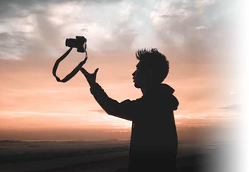 Chico lanzando al aire su cámara fotográfica al atardecer