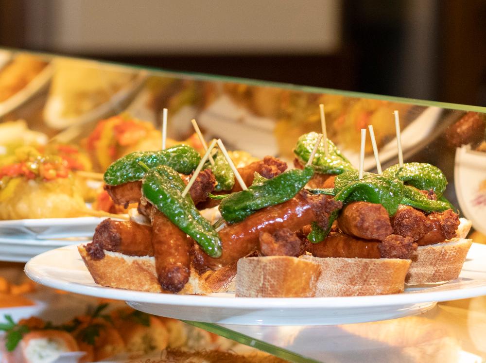 Plato con pinchos de chistorra y pimiento verde sobre rebanada de pan