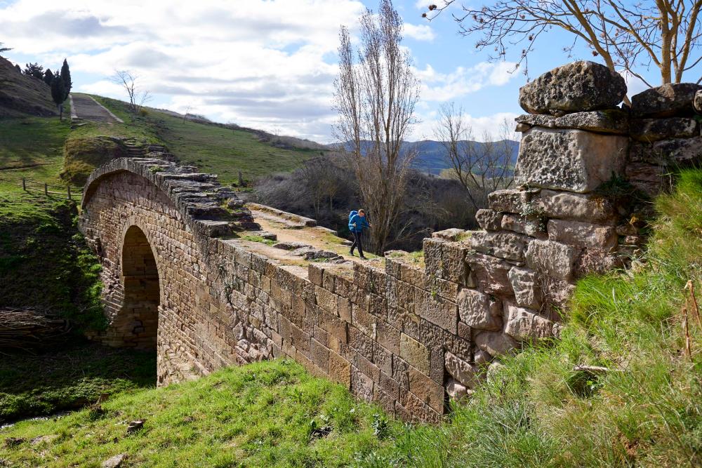 Un hombre andando sobre el puento romano de Cirauqui