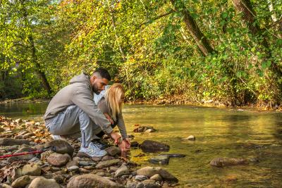Un chico y una chica, en cuclillas, en al orilla de un río tocando el agua con las manos