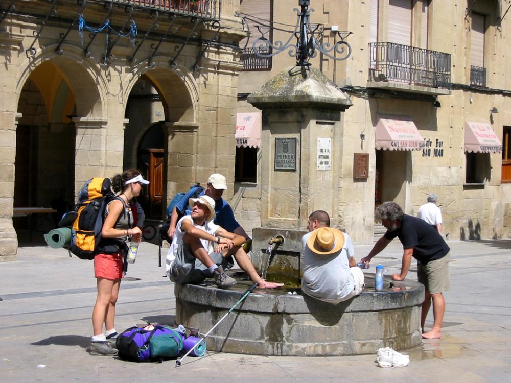 grupo de peregrinos sentados en la fuente de Viana refrescándose los pies