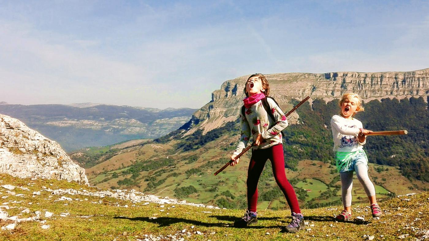 Two girls with sticks scream with Mount Beriain in the background